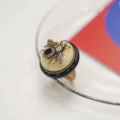 Bague "Reine Noire" en argent avec une abeille ornée d'une petite pierre noire sur une agate noire et une base crème.