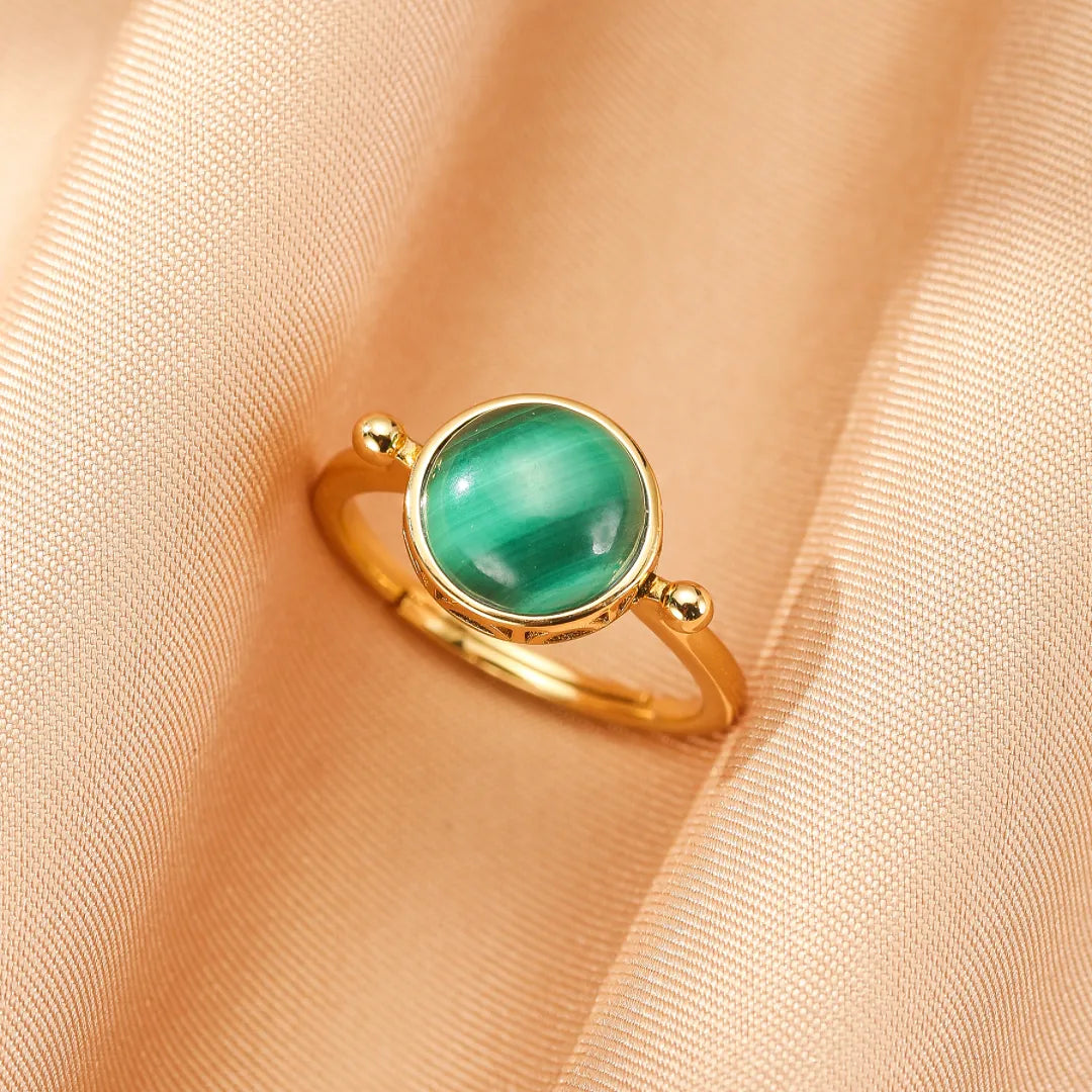 Bague ajustable en argent doré sertie d'une pierre de malachite verte aux reflets chatoyants, style antique, sur fond satiné.