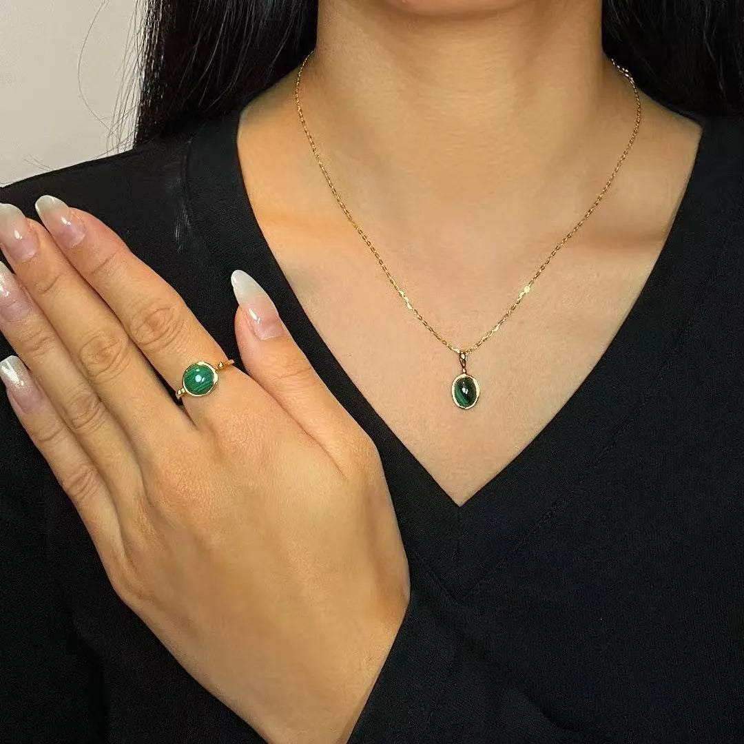Bague "Aura Antique" en argent doré avec une pierre de Malachite ronde, portée à l'annulaire, associée à un pendentif assorti.