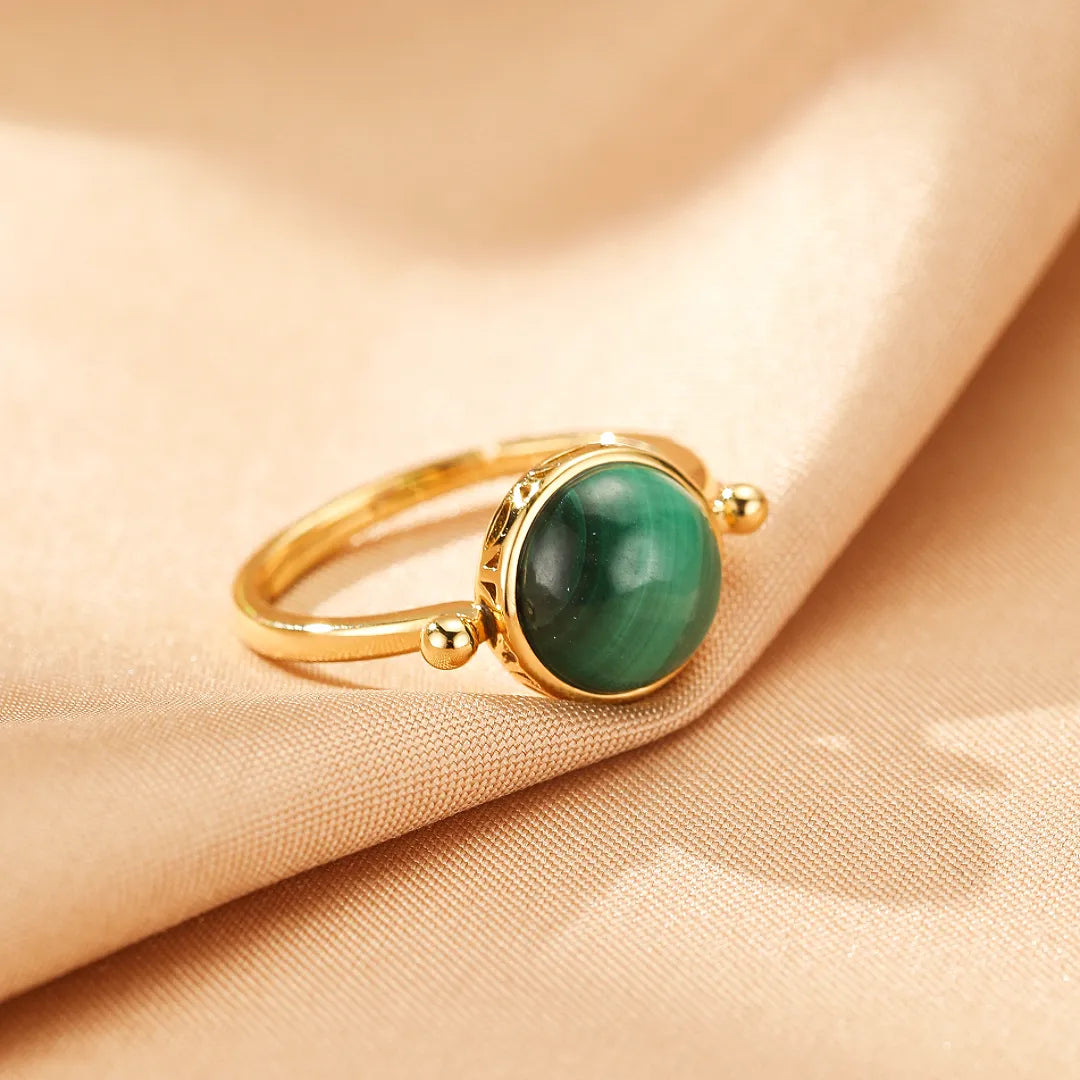 Bague en argent doré or sertie d'une pierre de malachite ronde et lisse, avec un design antique gravé sur le corps de la bague.