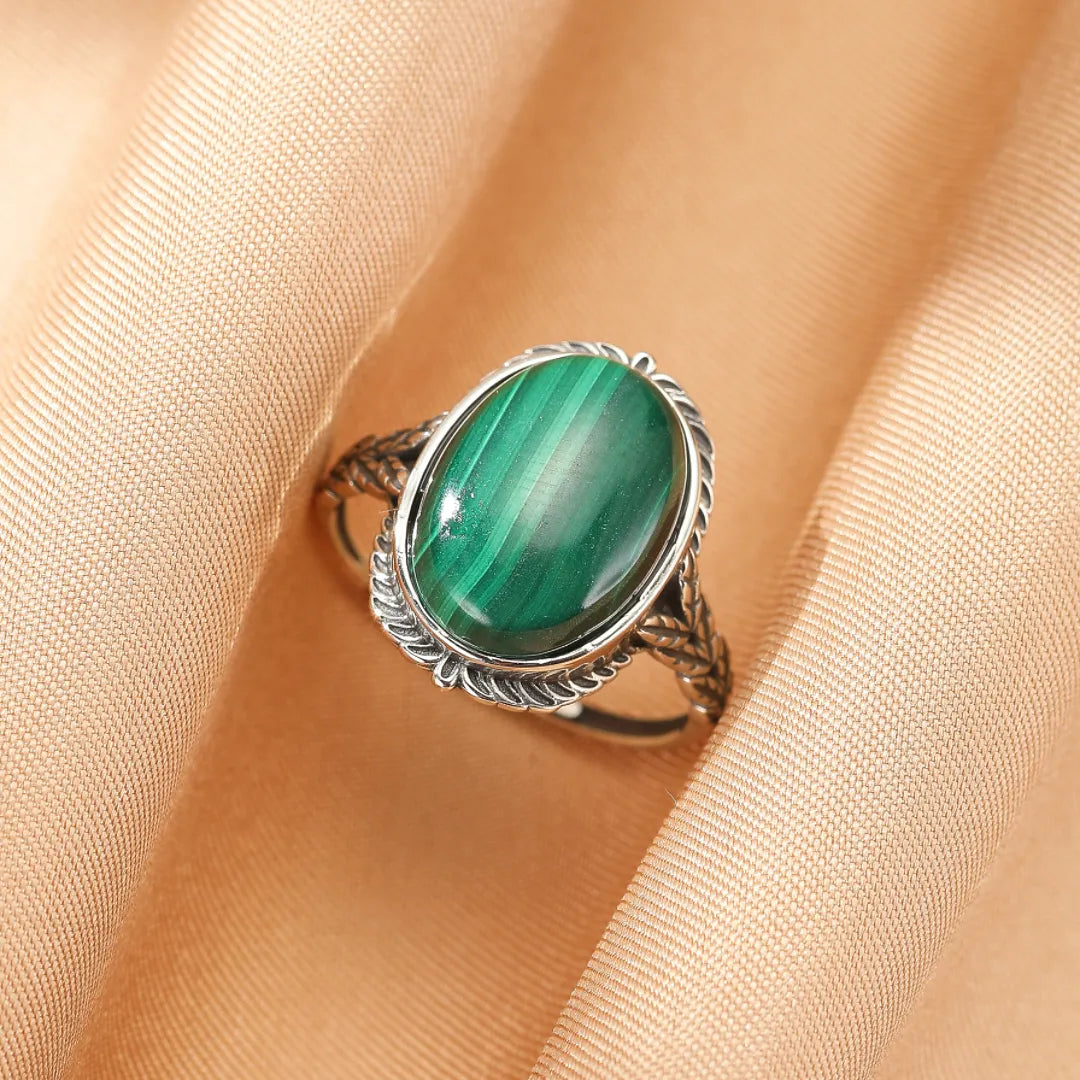 Bague en argent avec une grande malachite ovale au centre, ornée d'un motif torsadé et végétal sur l'anneau.