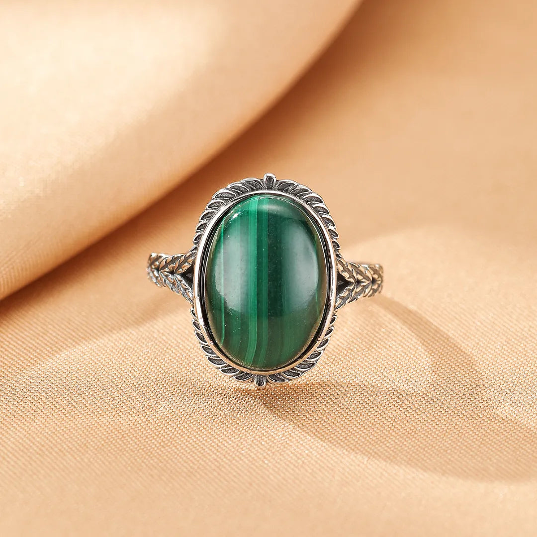 Bague en argent sertie d'une malachite ovale aux rayures vertes profondes, avec un design de feuillage gravé sur l'anneau.