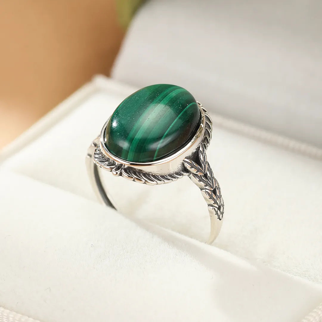 Bague en argent avec une grosse pierre de malachite ovale ornée de motifs végétaux sur l'anneau.