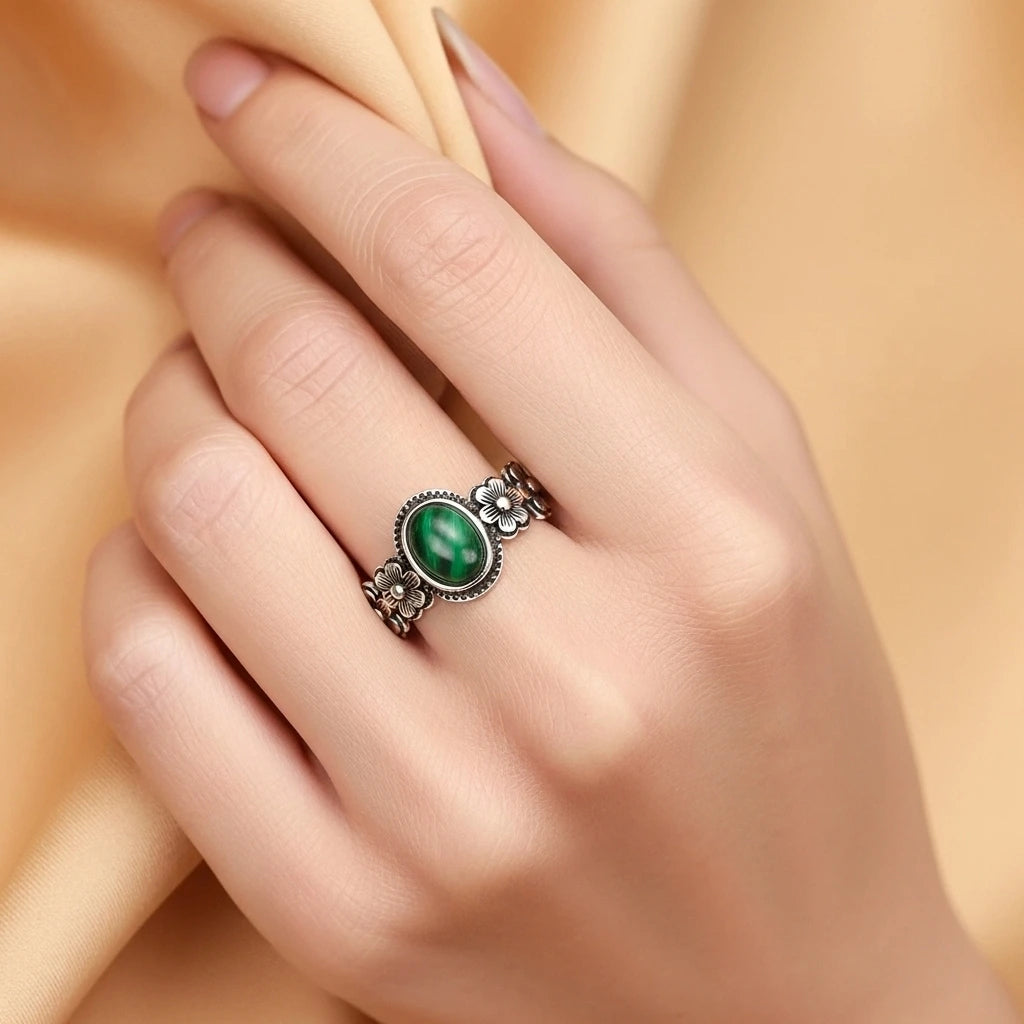 Bague en argent avec une malachite ovale au centre et des motifs floraux sur les côtés, portée à l'annulaire.