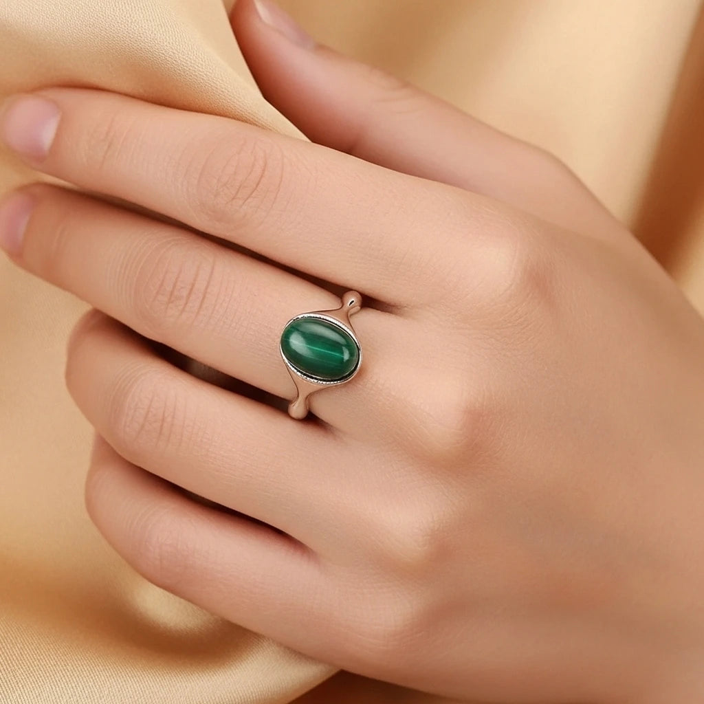 Bague en argent avec une pierre de malachite ovale au centre, portée à l'annulaire d'une main.