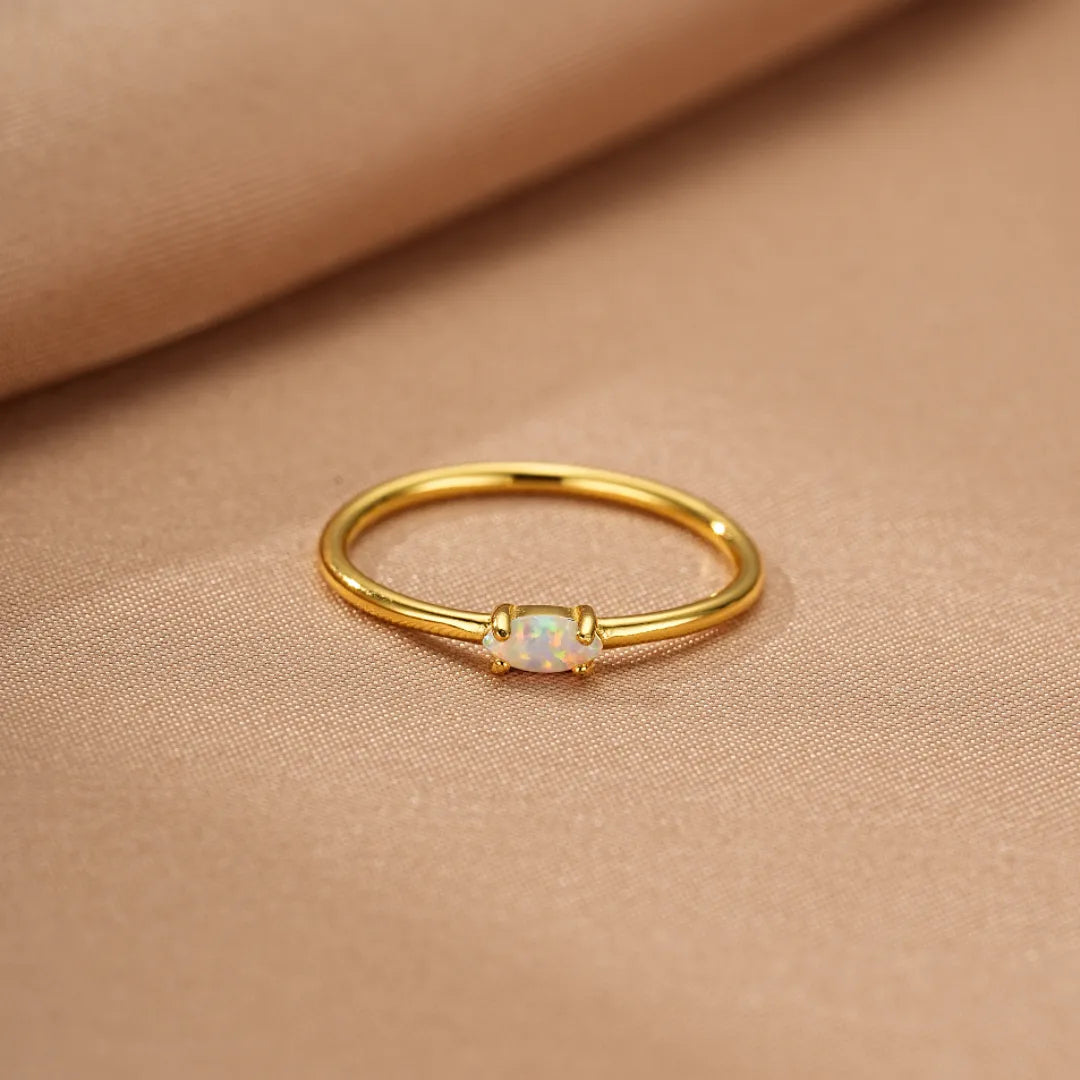 Bague fine en argent doré à l'or avec une petite opale rectangulaire blanche au centre, sur fond beige satiné.