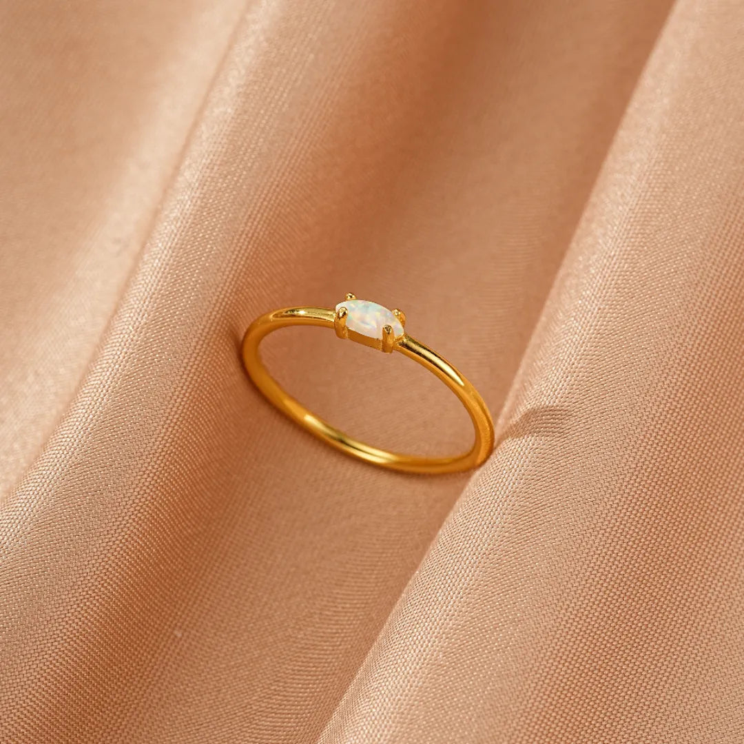 Bague fine en argent doré or avec une opale ovale blanche au centre, sur fond satiné.