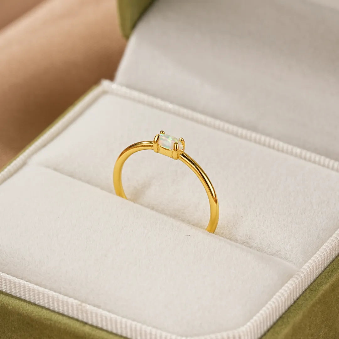 Bague en argent doré or avec une opale rectangulaire blanche au centre, présentée dans une boîte à bijoux verte.