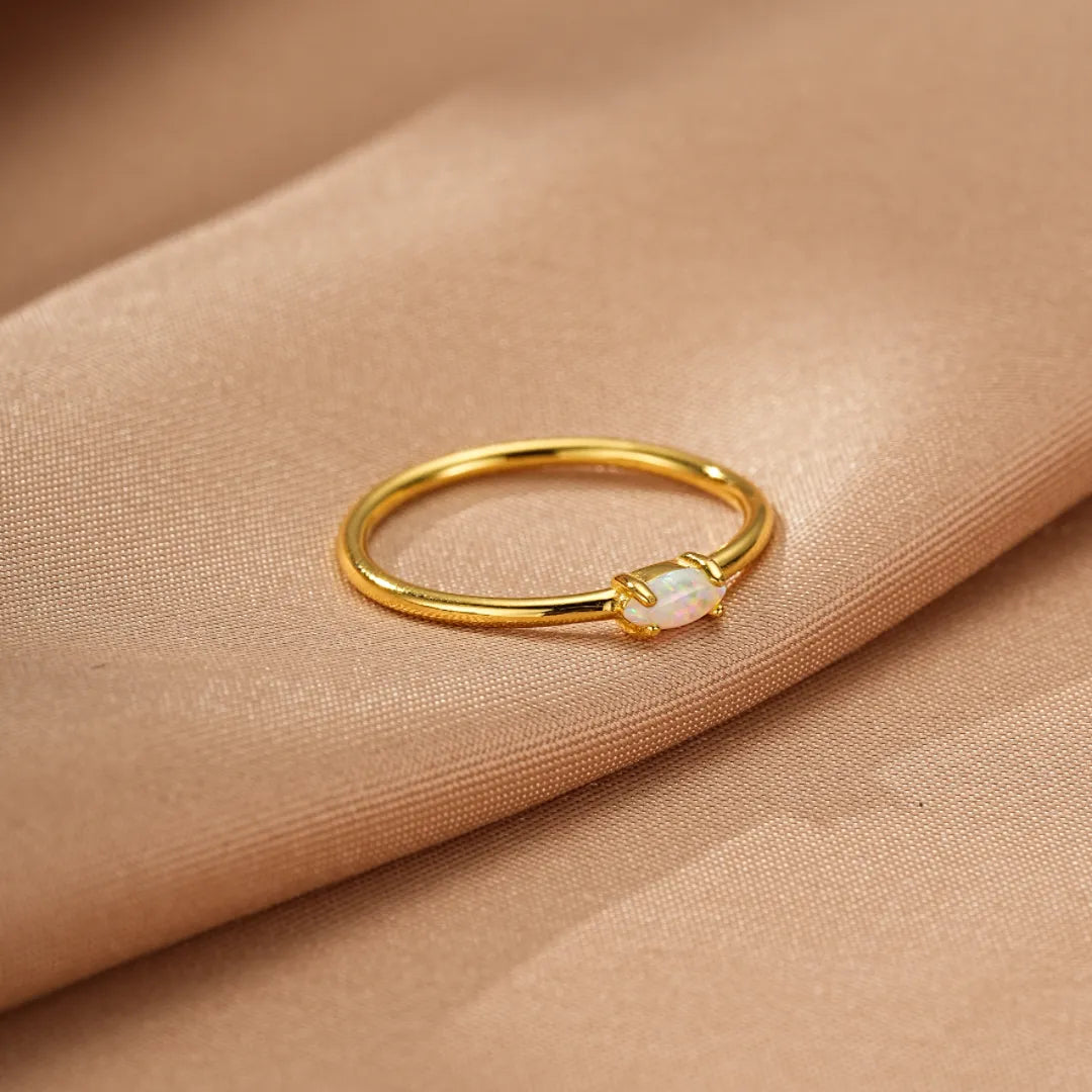 Bague Éclat Tendre en argent doré or, sertie d'une opale ovale blanche et lumineuse, posée sur un tissu satiné beige.