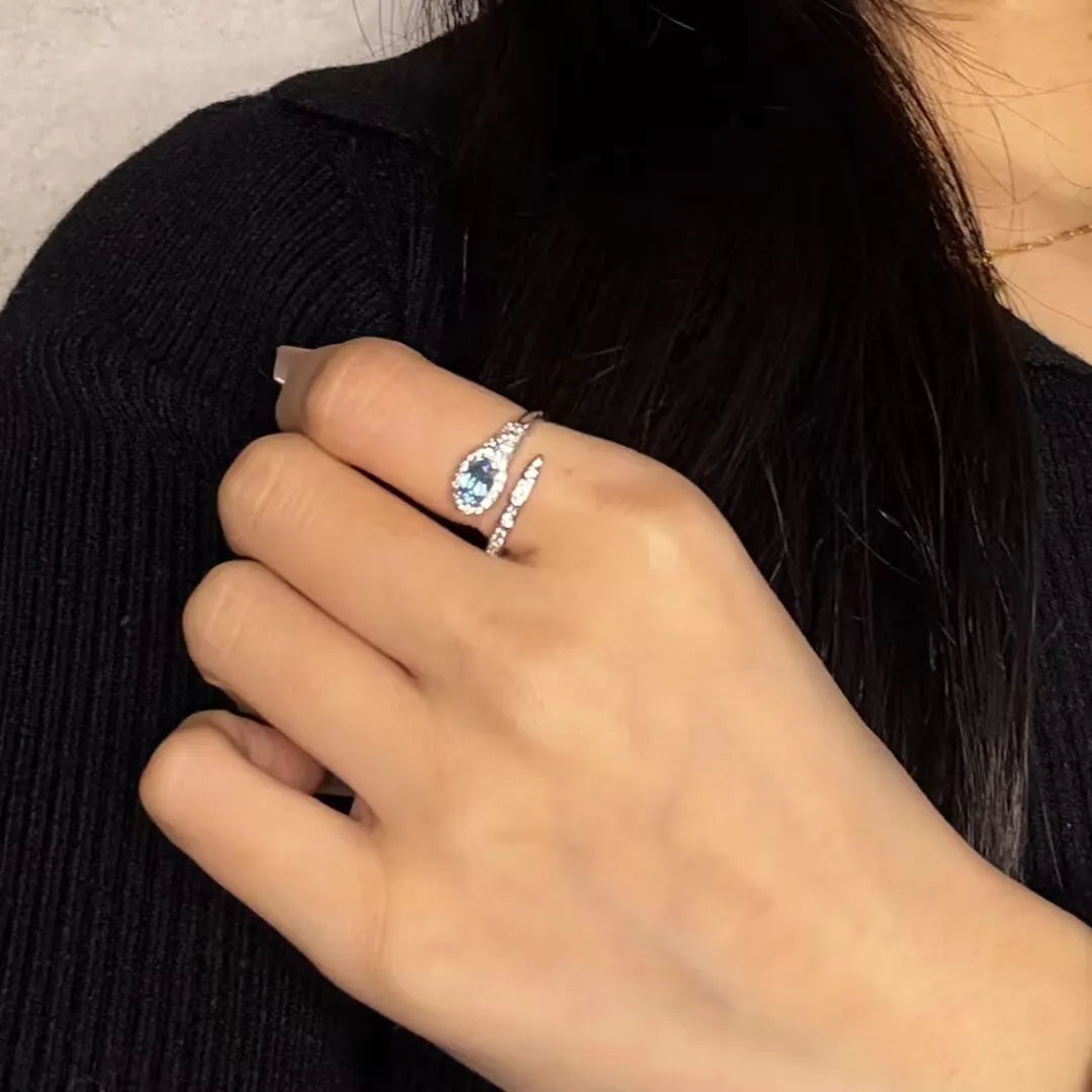 Bague serpent en argent 925 ornée d'une topaze bleue en forme de larme et de petits cristaux scintillants, portée à l'annulaire.