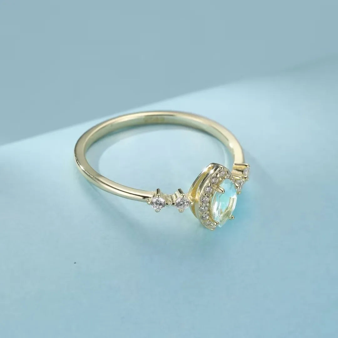 Bague en argent 925 sertie d'une topaze ovale bleutée entourée de petits zircons et de trois diamants sur le côté de l'anneau.