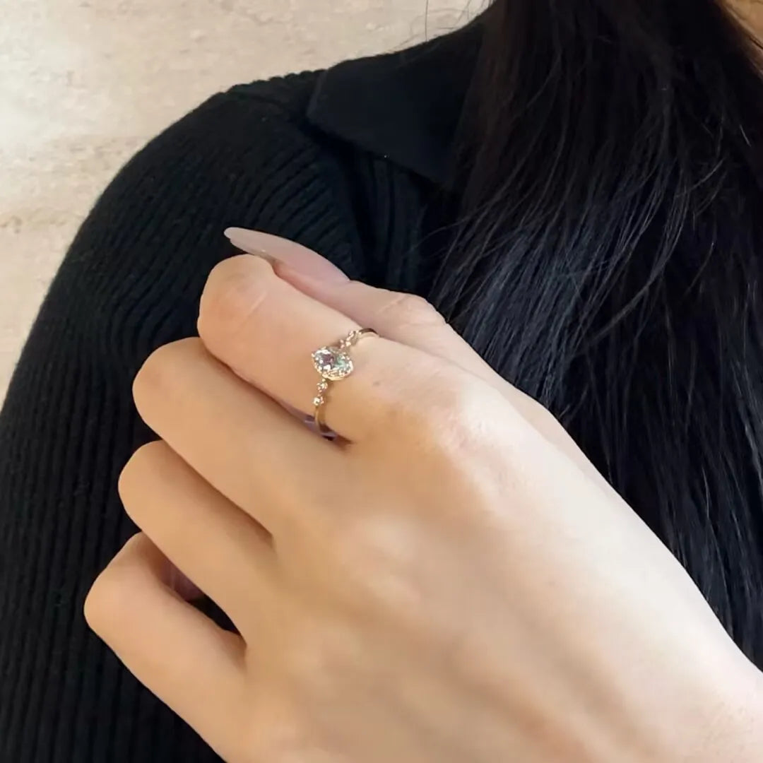 Bague en argent 925 avec une topaze bleue en forme de cœur et de petites pierres scintillantes sur le côté, portée à l'annulaire d'une main.
