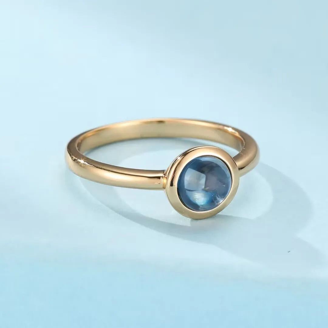 Bague en argent doré or avec une topaze bleue ronde sertie, style minimaliste et élégant.