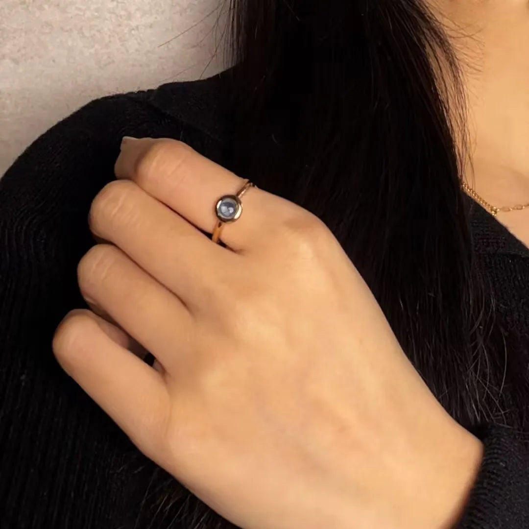 Bague "Éclat de l'Aube" en argent doré or, ornée d'une topaze bleue ronde sertie clos, portée au doigt d'une femme.