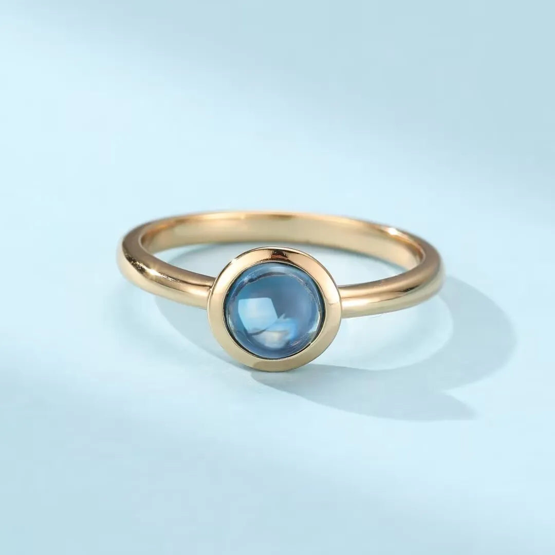 Bague en argent doré or sertie d'une topaze bleue ronde et lisse, style minimaliste.