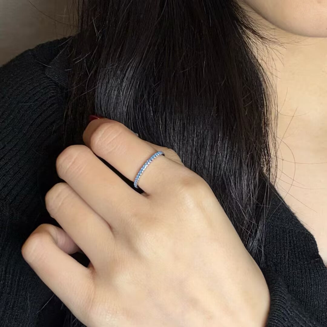 Bague fine en argent 925 sertie de petites pierres bleues lumineuses, portée à l'annulaire d'une main aux ongles soignés.