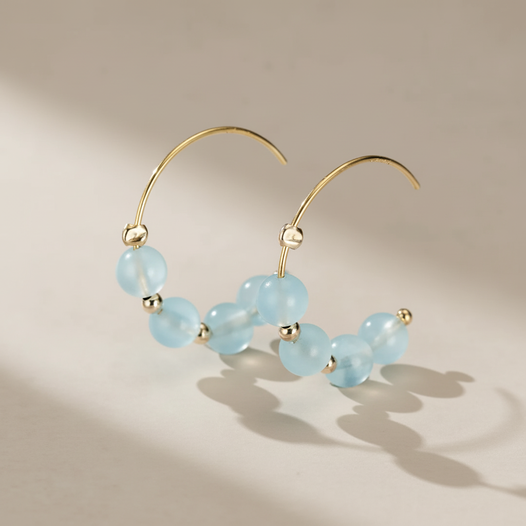 Paire de boucles d'oreilles créoles en or jaune serties de perles d'aigue-marine bleues claires et de petites perles dorées.