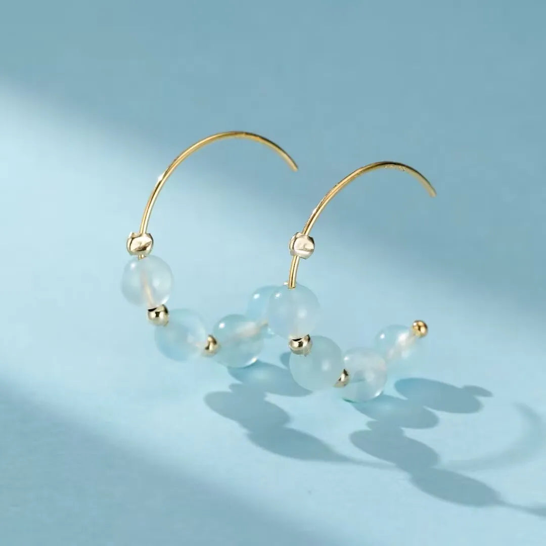 Boucles d'oreilles créoles dorées ornées de perles bleues claires en aigue-marine, style bohème chic.