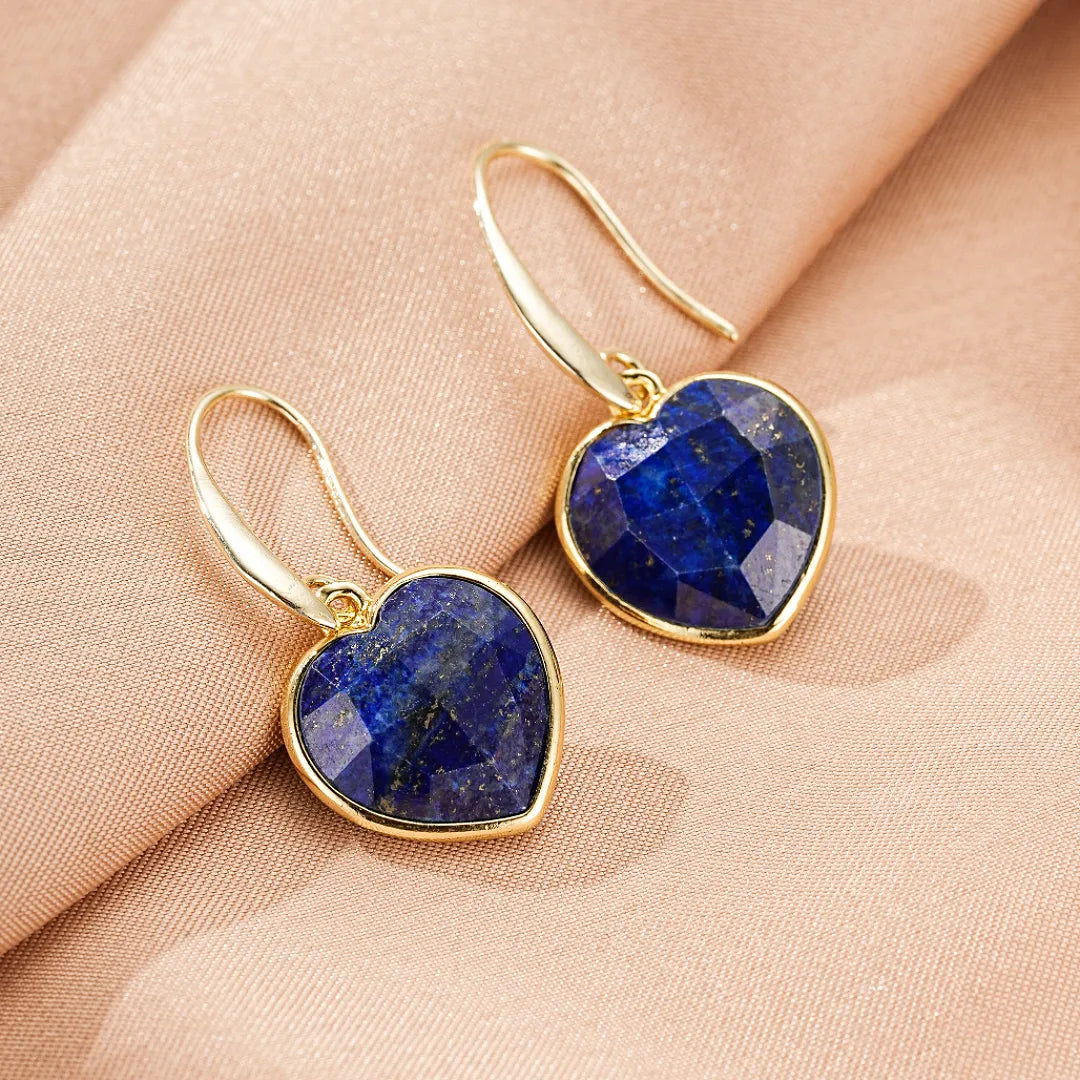 Boucles d'oreilles en forme de cœur en lapis lazuli, montées sur de l'or, sur un fond rose poudré.