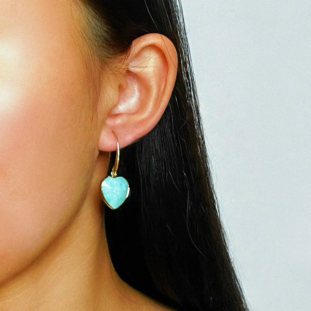 Boucle d'oreille cœur en amazonite bleu pâle avec monture dorée, portée à l'oreille d'une femme.