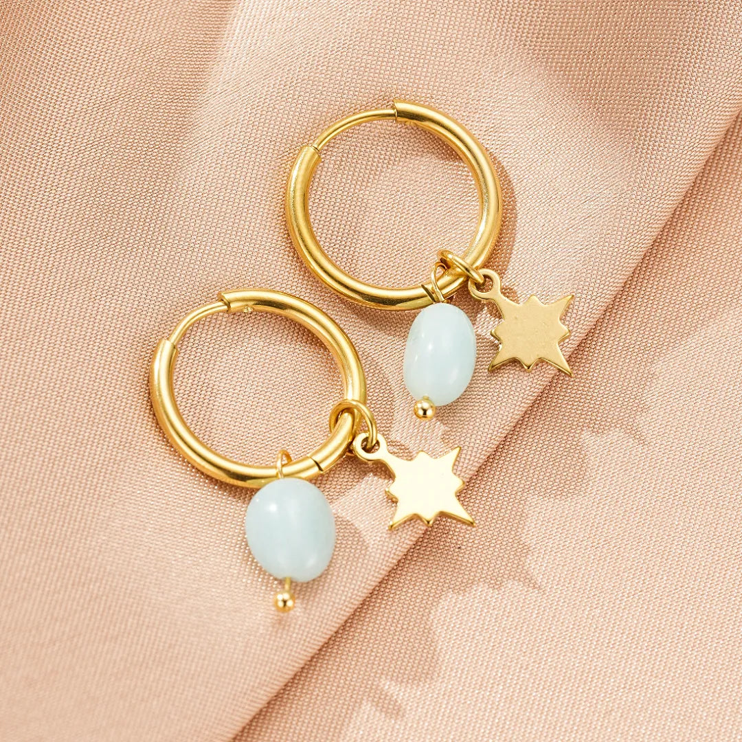 Boucles d'oreilles créoles dorées ornées d'une petite pierre bleu pâle et d'un breloque étoile dorée.