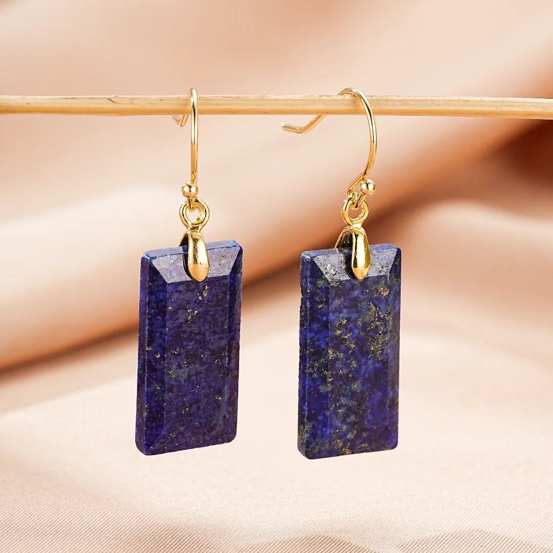 Paire de boucles d'oreilles rectangulaires en lapis-lazuli bleu profond avec inclusions dorées, suspendues à des crochets dorés.