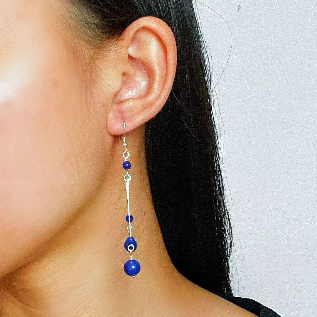 Boucles d'oreilles pendantes en argent avec des perles rondes de lapis-lazuli et une barre argentée, portées par une femme.