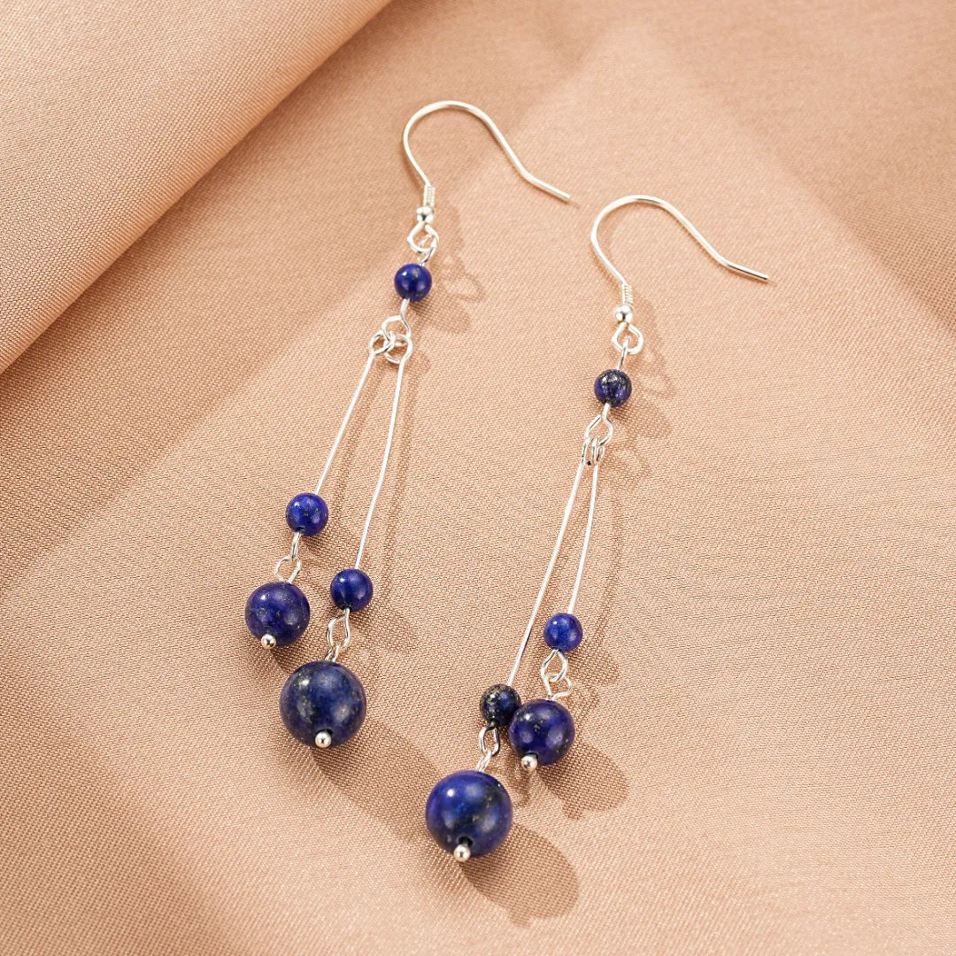 Boucles d'oreilles pendantes en argent ornées de perles rondes de lapis-lazuli de différentes tailles, suspendues à de fines chaînettes.