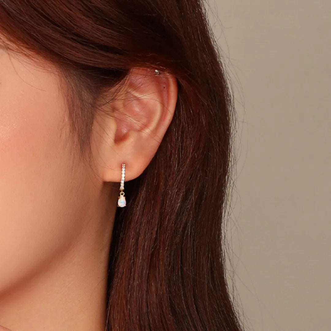 Boucle d'oreille "Charme Astral" en argent doré or avec une petite opale blanche en forme de goutte sertie de cristaux brillants.