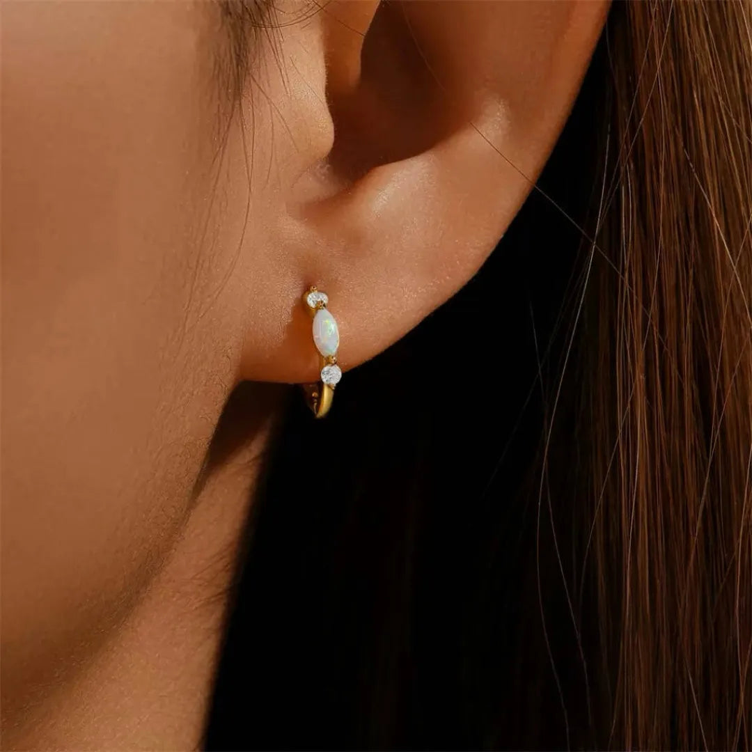 Boucle d'oreille créole en argent avec une opale centrale et deux petits diamants de chaque côté, portée à l'oreille.