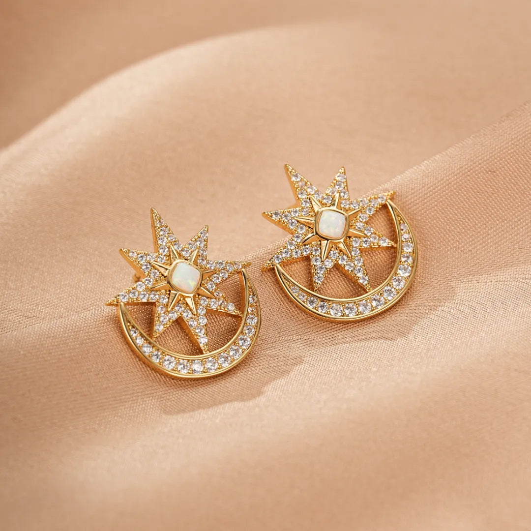 Boucles d'oreilles dorées en forme d'étoile ornée d'une opale centrale et d'un croissant de lune serti de zirconiums scintillants, posées sur un tissu satiné beige.