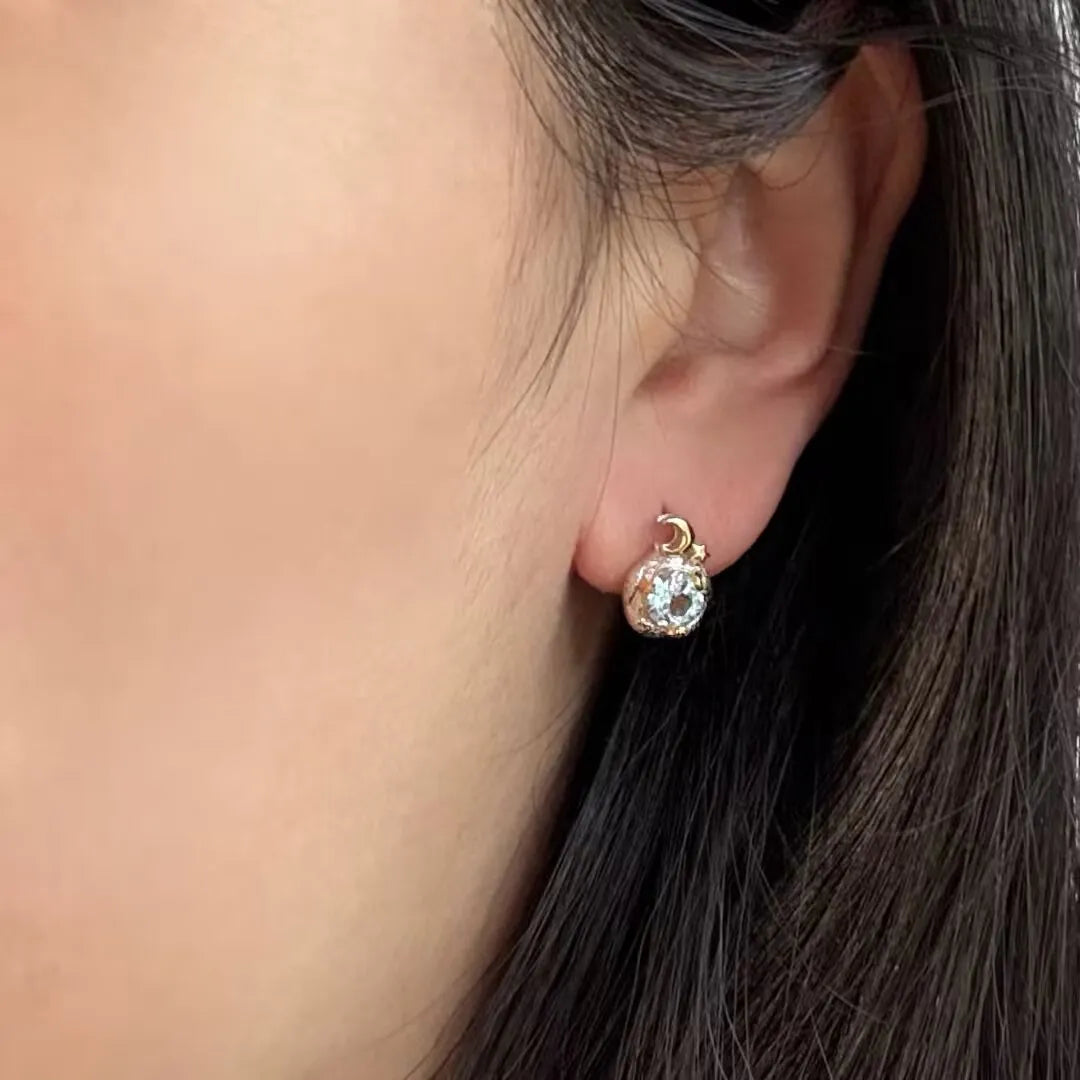 Boucle d'oreille argent 925 "Charme Céleste" avec une topaze bleue sertie sur un design sphérique ajouré, accrochée à une petite bélière en argent en forme de croissant de lune.