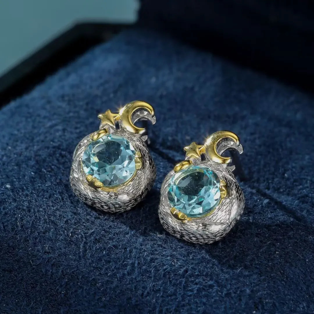 Paire de boucles d'oreilles "Charme Céleste" en argent 925 serties de topazes bleues rondes, ornées d'un croissant de lune et d'étoiles dorées.