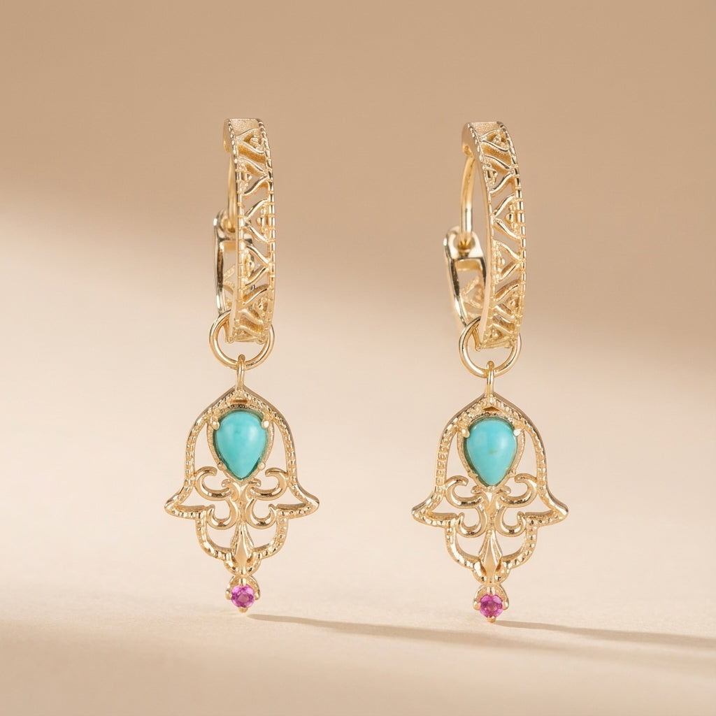 Boucles d’oreilles pendantes en argent doré ornées d’une turquoise en forme de goutte et d’un petit rubis, avec un motif de main de Fatima ajouré et des détails géométriques sur les anneaux.
