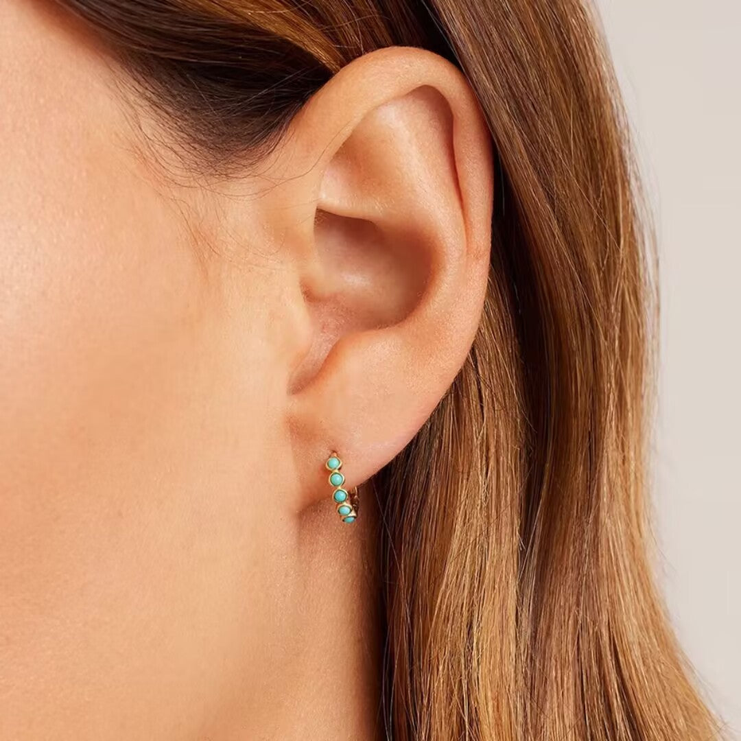 Boucle d'oreille créole en argent doré, ornée de petites pierres turquoise bleues, portée à l'oreille.