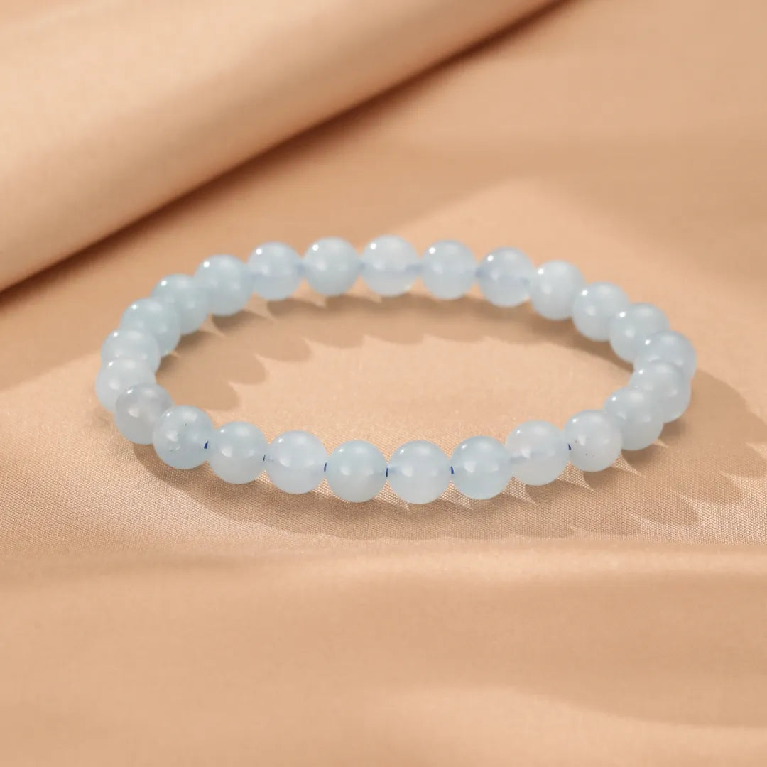Bracelet "Brise Marine" fait de perles d'aigue-marine bleues pâles sur un fond beige satiné.
