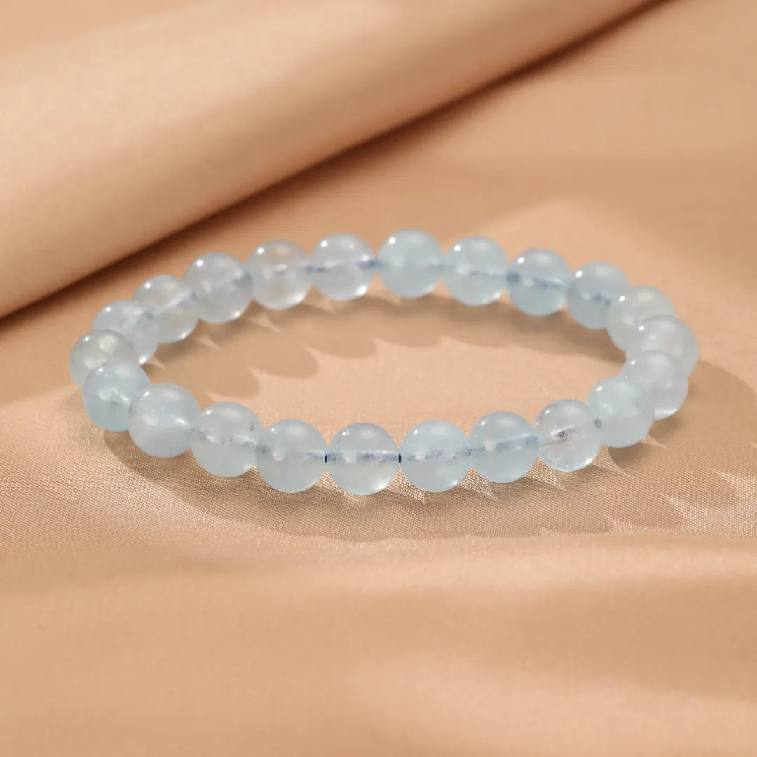 Bracelet "Brise Marine" fait de perles d'aigue-marine bleues pâles, posé sur un tissu beige satiné.