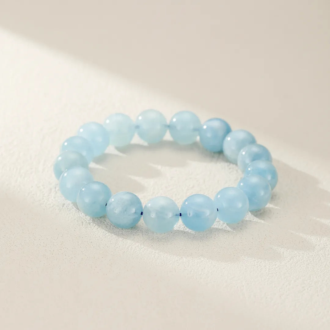 Bracelet en Aigue Marine "Douceur Calmante" composé de perles bleues claires et translucides sur un fond blanc texturé avec des ombres douces.