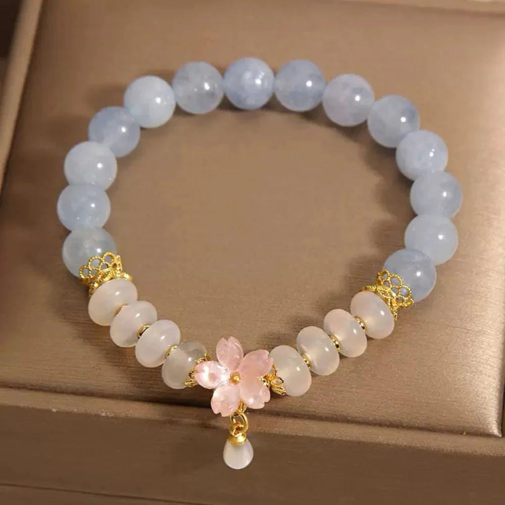 Bracelet "Pureté de Matin" fait de perles bleues d'aigue-marine, de perles blanches d'agate et d'un pendentif fleur de cerisier rose avec une gouttelette.