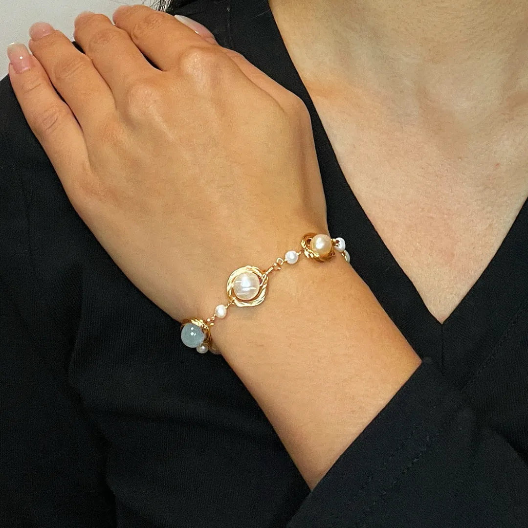 Bracelet fin en or avec des perles d'eau douce et une pierre d'aigue-marine bleue, porté au poignet d'une femme.