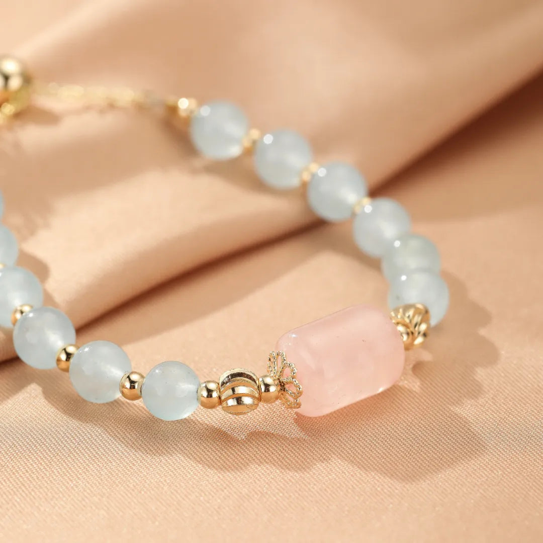 Bracelet "Souffle Doux" fait de perles d'aigue-marine bleu pâle et d'une perle centrale en quartz rose, avec des accents dorés.