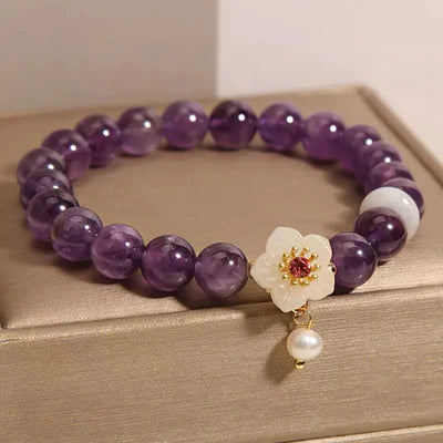 Bracelet "Fleur d'Harmonie" fait de perles d'améthyste violettes, de jade blanc et orné d'une breloque fleur blanche avec une perle blanche suspendue.