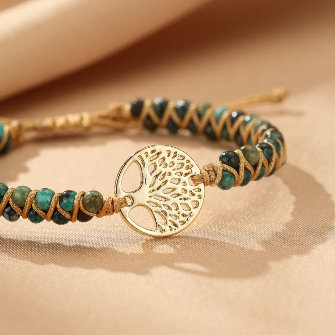 Bracelet Arbre de Vie en jaspe africain avec un pendentif arbre de vie doré et des perles vertes et bleues enroulées sur un cordon marron.