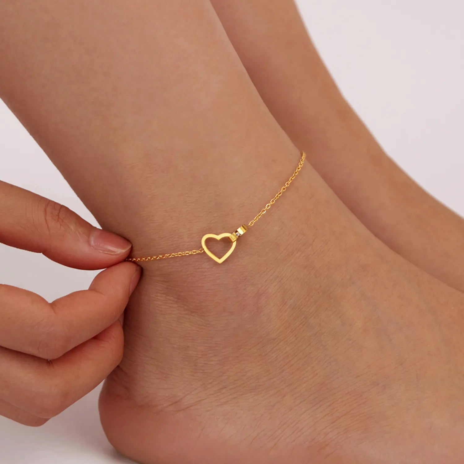 Bracelet de cheville doré avec un pendentif en forme de cœur ouvert, porté sur la cheville d'une femme.