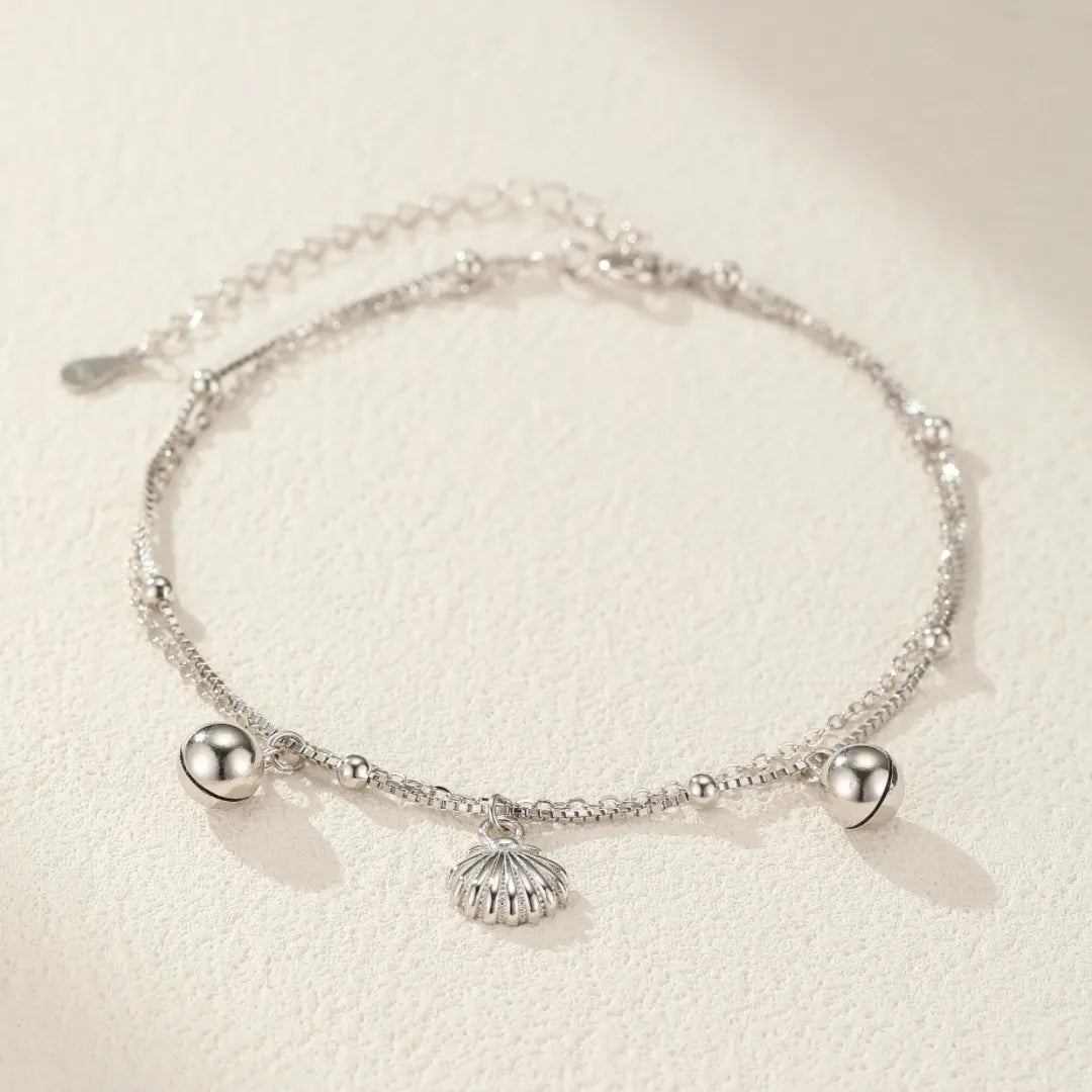 Bracelet de cheville double chaîne orné d'un pendentif coquillage stylisé et de deux petites billes argentées, le tout en argent 925.