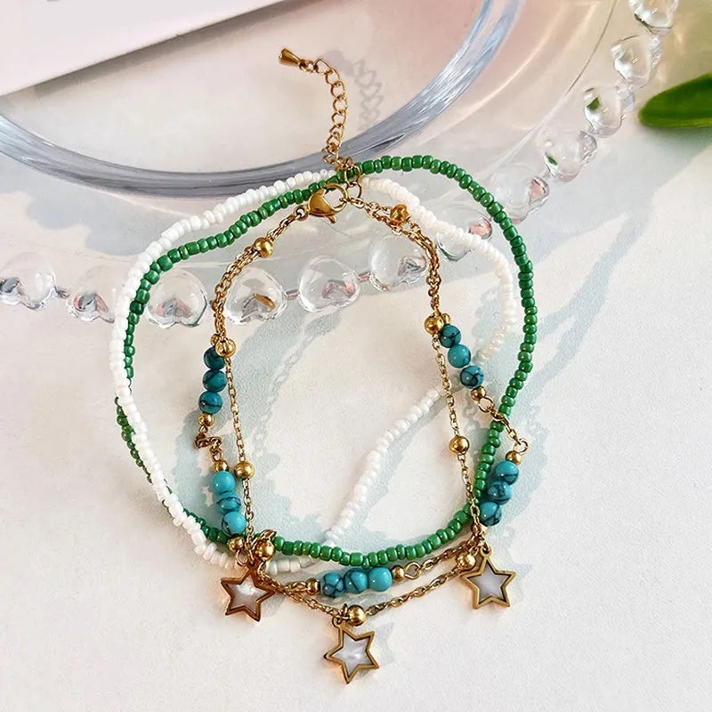 Ensemble de trois bracelets de cheville, deux avec des perles blanches et vertes et un avec des perles bleues turquoise et des breloques étoiles dorées.