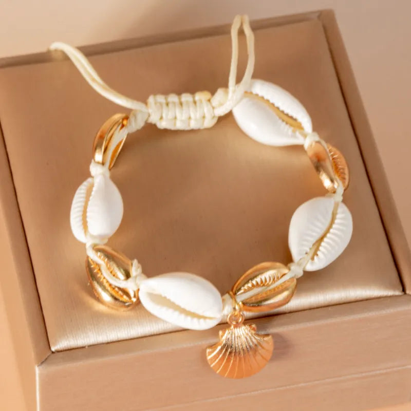 Bracelet de cheville "Protection Maritime" orné de coquillages cauris blancs et de perles dorées, avec un pendentif en forme de coquillage doré.