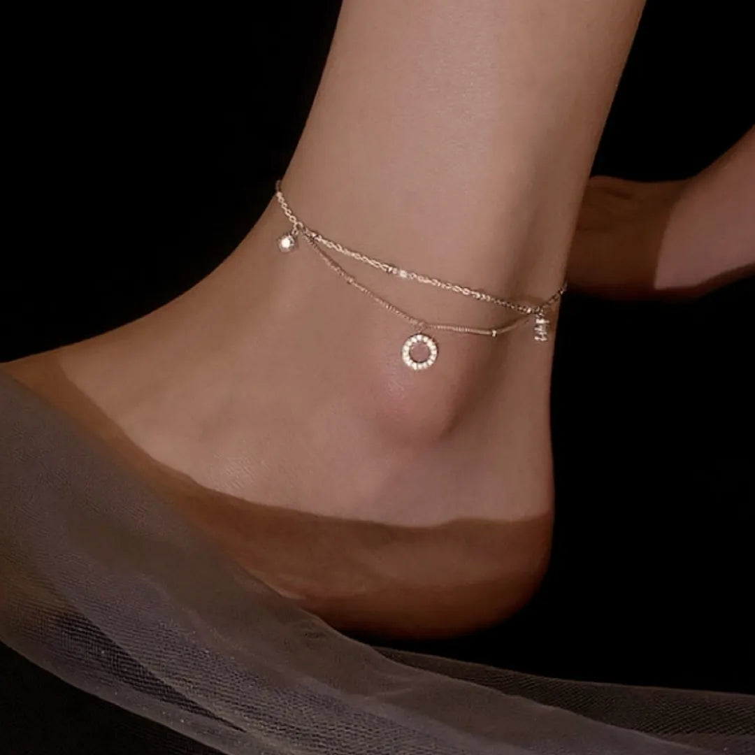 Bracelet de cheville double chaîne "Élégance Brillante" en argent 925, orné de deux breloques scintillantes : un petit cercle pavé de zircons et une petite boule lumineuse.