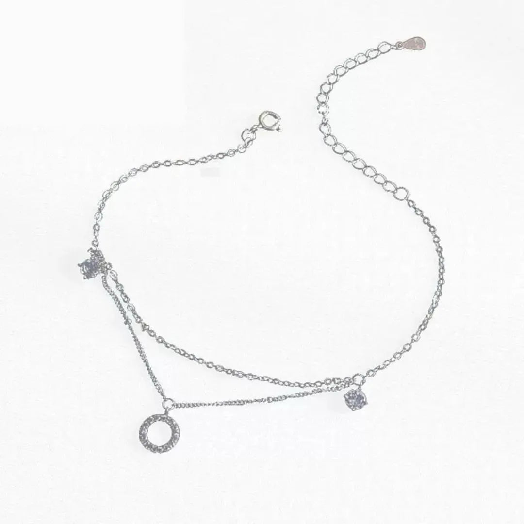 Bracelet de cheville double chaîne en argent 925 orné d'un pendentif rond serti de zirconium et de deux petits carrés brillants.