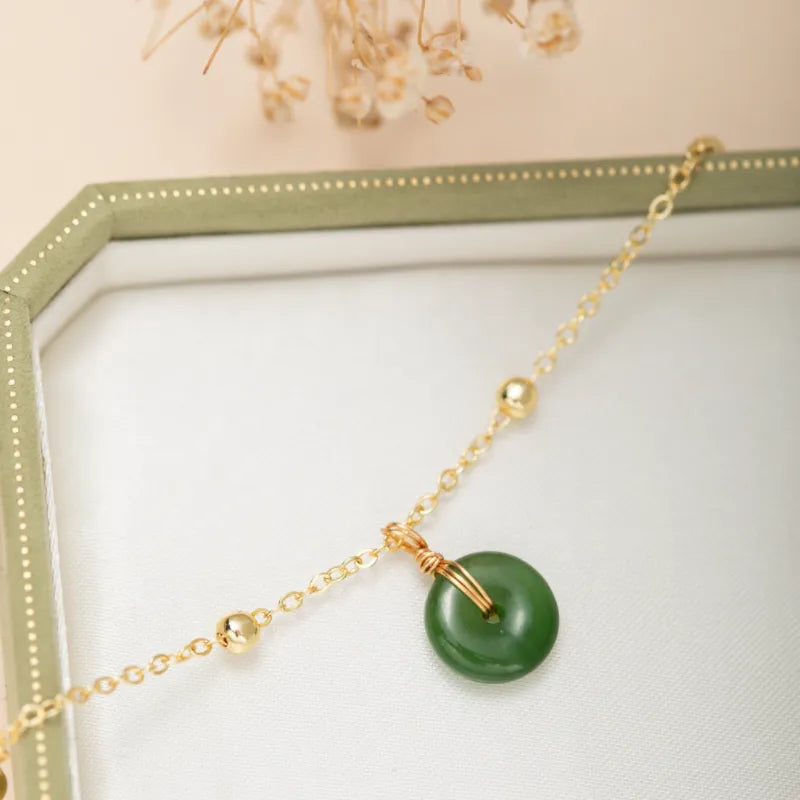 Bracelet de cheville en argent doré avec une pierre de jade verte ronde suspendue à une fine chaîne ornée de petites perles dorées.